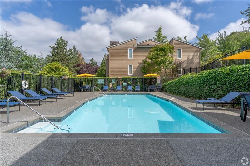 A large swimming pool surrounded by a black fence and lounge chairs.